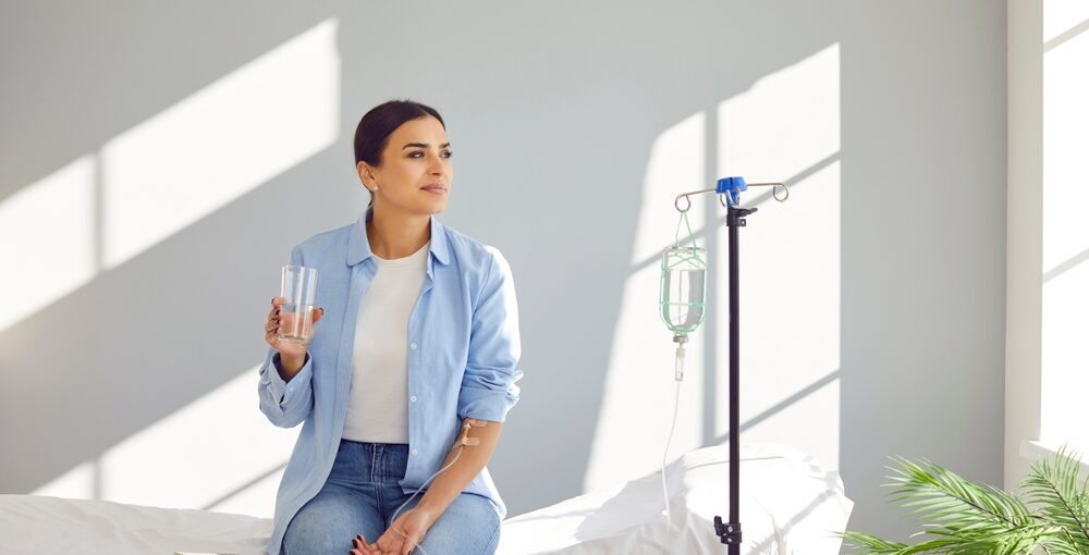 Woman receiving IV drip therapy in Saraland AL while holding a glass of water