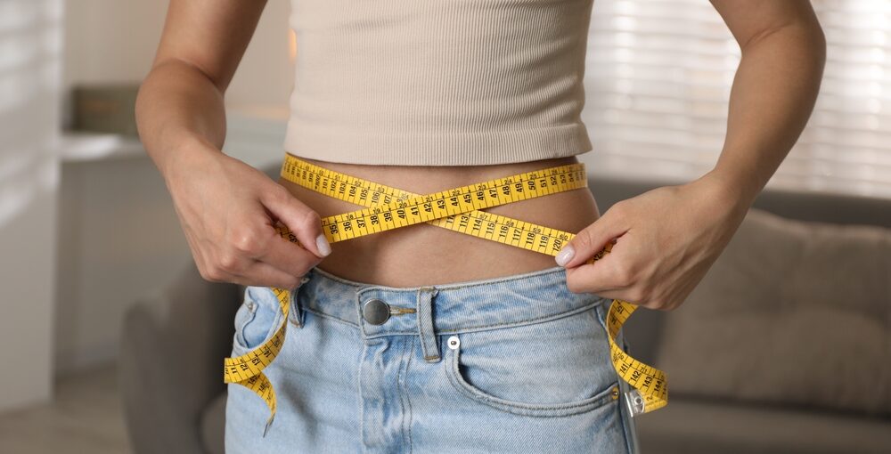 Person measuring waistline with tape measure during medical weight loss in Saraland AL