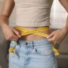 Person measuring waistline with tape measure during medical weight loss in Saraland AL