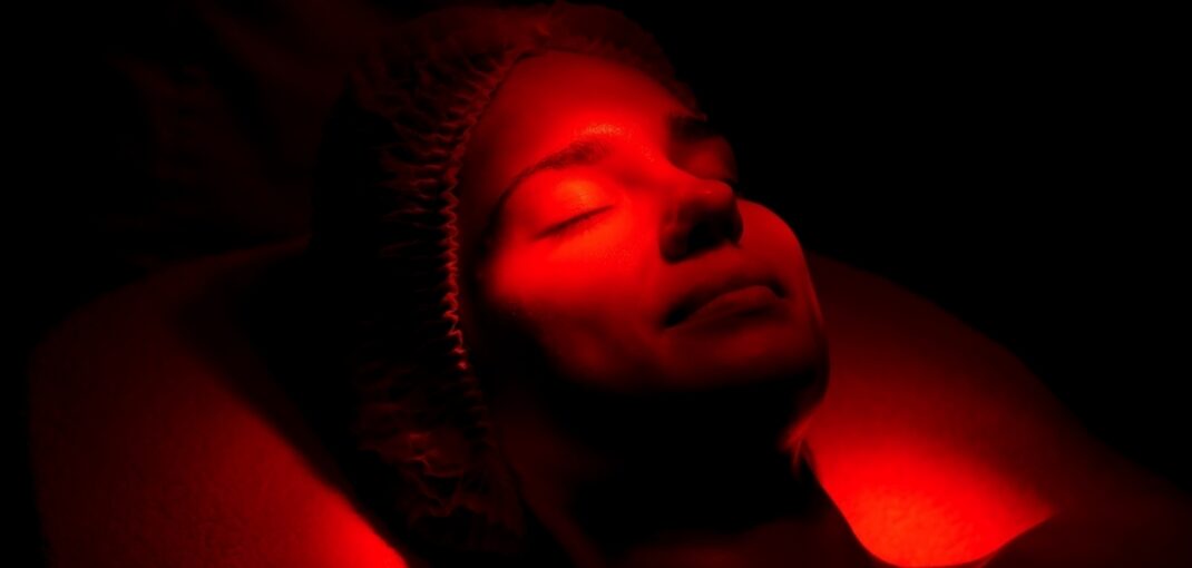 Woman with eyes closed under warm red glow during red light therapy and sleep support session at a wellness clinic