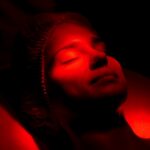 Woman with eyes closed under warm red glow during red light therapy and sleep support session at a wellness clinic