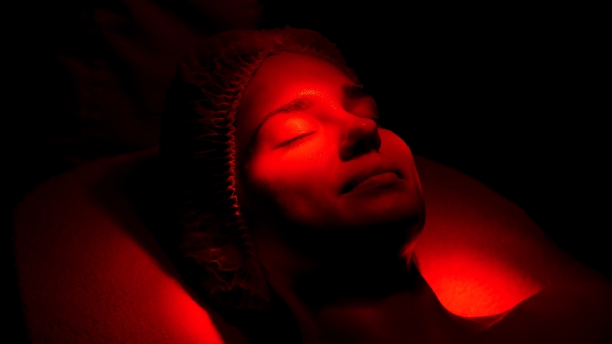 Woman with eyes closed under warm red glow during red light therapy and sleep support session at a wellness clinic
