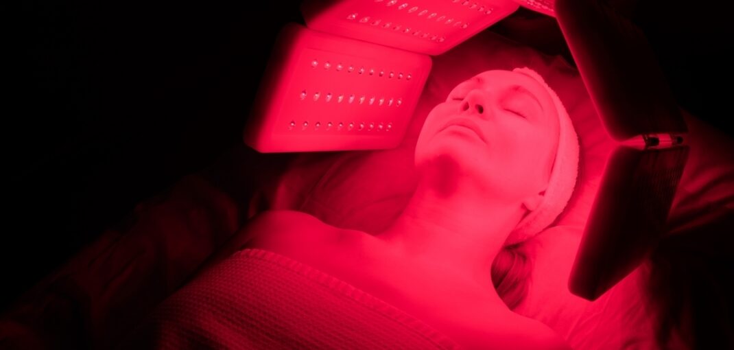 Woman lying under red light therapy session panels with eyes closed at a wellness clinic