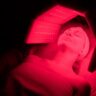 Woman lying under red light therapy session panels with eyes closed at a wellness clinic
