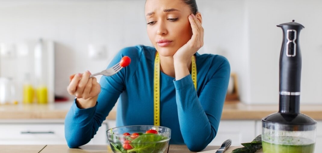 Frustrated woman with measuring tape eating a salad representing stress and weight loss challenges