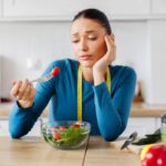 Frustrated woman with measuring tape eating a salad representing stress and weight loss challenges