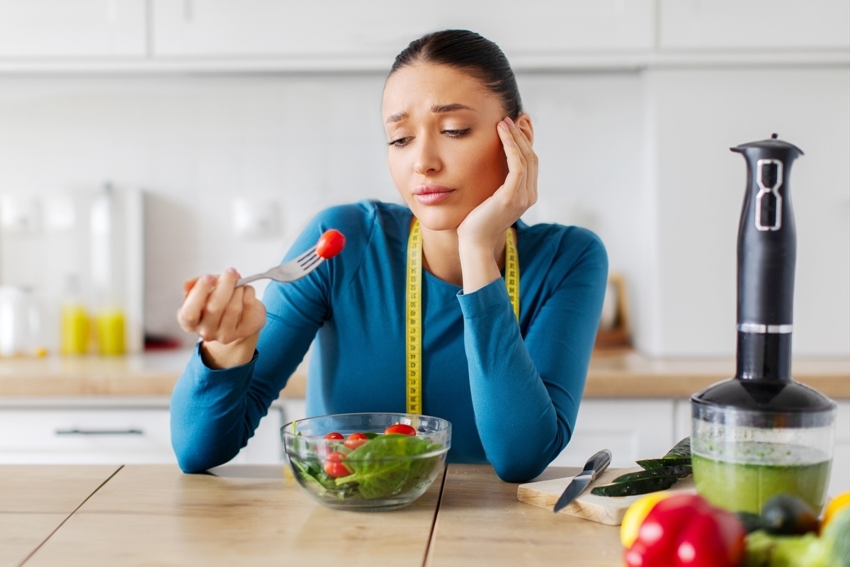 Frustrated woman with measuring tape eating a salad representing stress and weight loss challenges